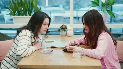Young Women Discussing Over a Smartphone in a Cafe