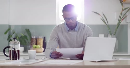 Man Reviews Documents at Kitchen Desk with Laptop
