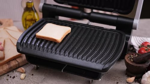 Woman Cooking Toasts of White Bread in Electric Grill at Domestic Kitchen Table