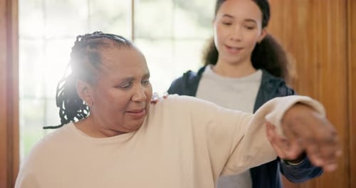 Young Adult Assists Senior with Arm Stretching Indoors