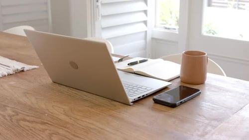 Laptop, smartphone, notebook, and coffee mug on wooden table in home office