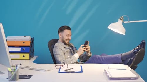 Smiling Businessman Relaxing at Desk with Smartphone