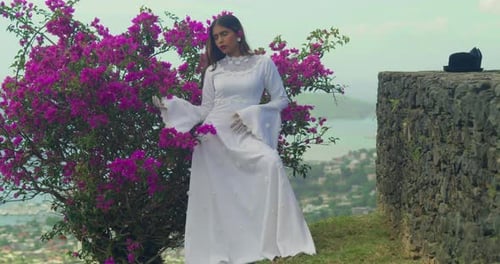 A young girl in a vintage bridal dress leaning against the weathered walls of a fort.