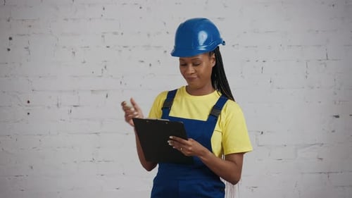 Medium Video of a Darkskinned Young Female Construction Worker Holding a Planchette Folder Writing