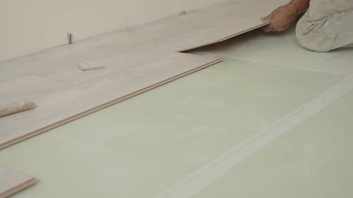 A Worker Carefully Lays Down Laminate Flooring in a Residential Space Ensuring Precise Placement The