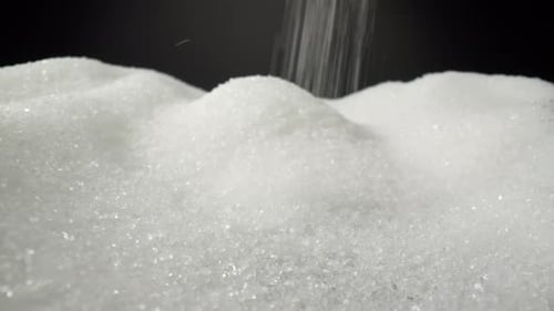 Weißer Zucker fällt zart auf einen glatten schwarzen Hintergrund