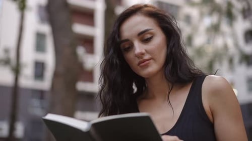 Woman Reading Book Outdoors in Urban Environment