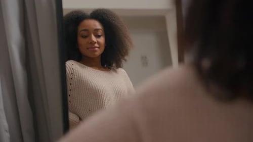 Glückliche, sorglose, hübsche, attraktive Afroamerikanerin, die zu Hause in Spiegelbild schaut