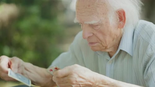 Old man playing cards in the city park with someone, arranging cards, Close up shot