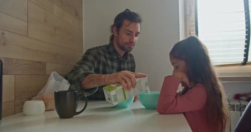 Happy Brunette Man Father in a Green Checkered Shirt Pours Milk Into Blue Plates for Himself and His