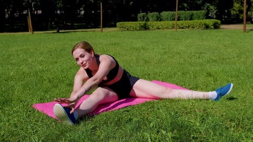 Woman Stretching Legs on Yoga Mat in Park