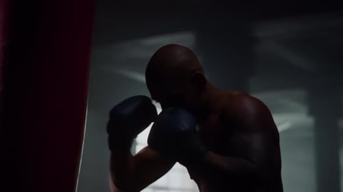Portrait Strong Man Hitting Punching Bag in Boxing Gloves. Close Up African
