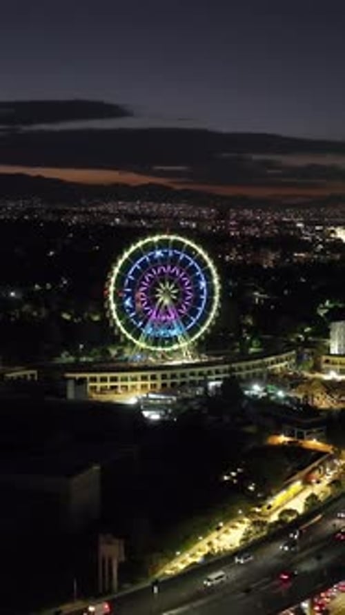 Vertical aerial view orbiting the ferris wheel of Aztlan Park, night in CMDX