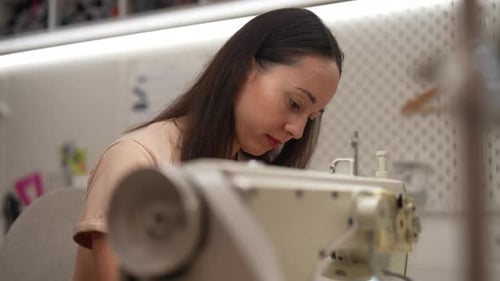 Closeup Side View of Focused Seamstress Using Sewing Machine Creating Garments in Bright Workshop