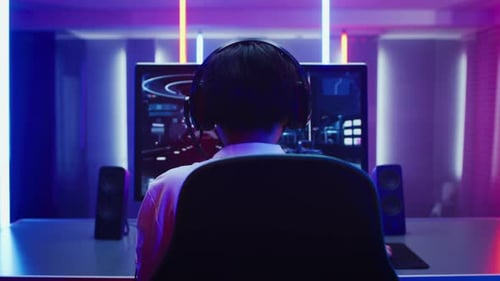Back View Zoom Out Shot of the Professional Gamer Playing in First-Person Shooter Online Video Game