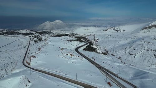 Aerial View of Winding Highway Through Snow-Covered Mountains