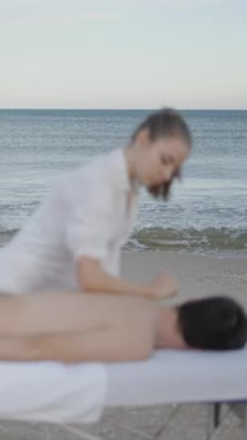 Man Lies Down on Massage Table at the Beach Unfocused with the Sea on Movement in the Background
