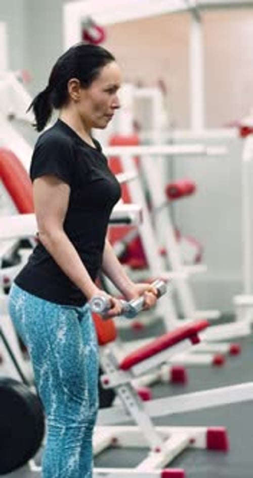 A Fit Middle Aged Woman Training Biceps with Dumbbells During an Intense Gym Workout