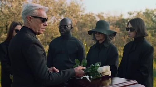Senior Man Putting Rose Blossoms on Wooden Coffin at Funerals