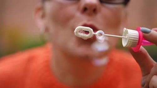 Gros plan : une femme méconnaissable portant des lunettes de soleil et un sweat-shirt orange fait des bulles de savon pendant