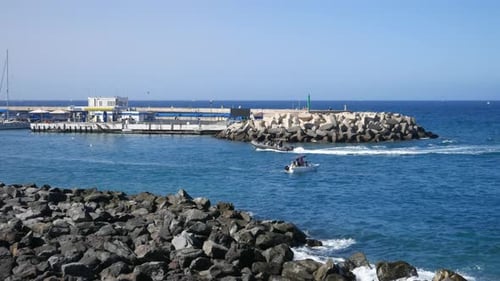 Une scène de port côtier avec des bateaux naviguant près d'une jetée et d'un brise-lames sous un ciel bleu clair
