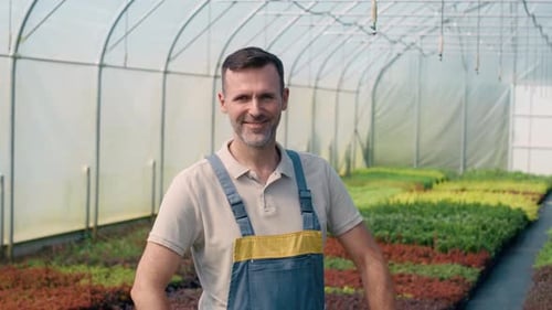 Smiling Gardener in Greenhouse with Rows of Potted Plants