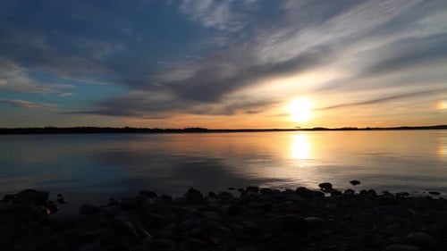 sunrise time lapse with clouds passing in front of an orange sun over a large lake
