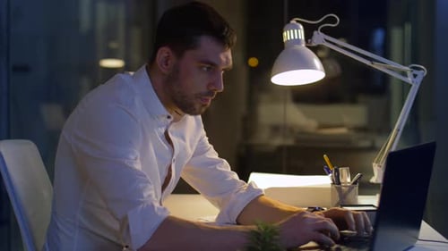 Businessman typing on laptop working late at night in a modern office