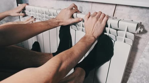 Hands and Feet are Heated on the Heating Radiator of the House Couple Keep Warm