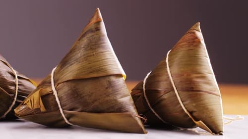 Hand Holding Zongzi (Rice Dumpling) with Savoury Fillings Wrapped in Bamboo or Reed Leaves