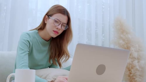 Young asian woman wearing glasses sitting on sofa worried with bills about financial and stress.