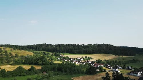 Drone flying over village with small houses at countryside with by green hills