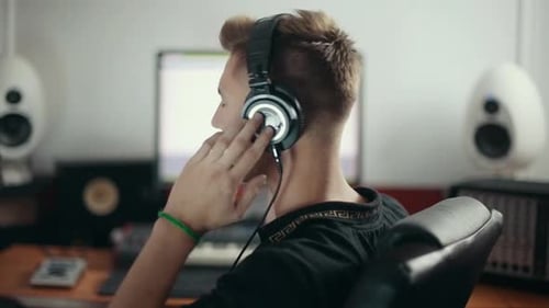 Young sound engineer listening to the music in headphones and turning face back to the camera