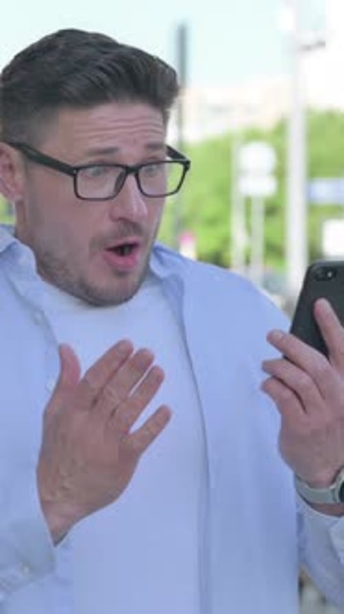 Surprised Man Reacting to News on Smartphone Outdoors