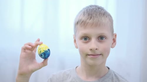 Easter Boy Holds in His Hand an Easter Egg Painted in Yellow and Blue Colors