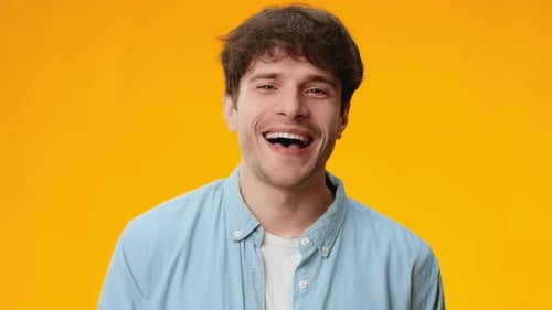 Man Smiles and Poses Against a Bright Orange Background in a Cheerful Setting During a Video Shoot