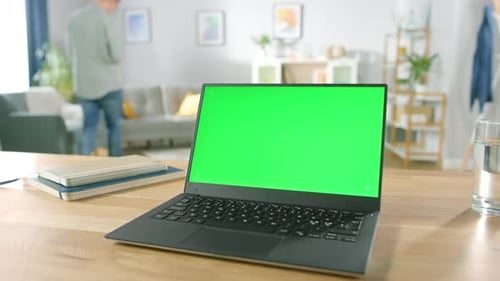 Modern Laptop with Green Mock-up Screen Display Standing on the Desk in the Cozy Living Room. Man w