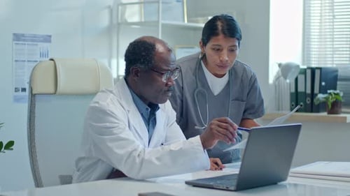 Doctor Explaining Job Tasks on Laptop Screen to Nurse in Clinic