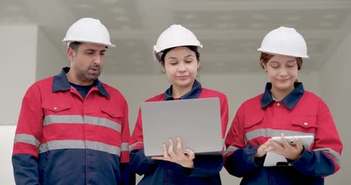 Asian woman engineer uses laptop while male contractor points at digital plan, second woman