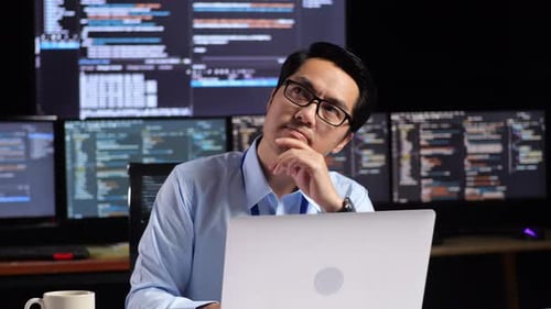 Programmer Thinking About Something While Writing Code By A Laptop Using Multiple Monitors