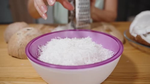 La mujer ralla el coco en trozos y los vierte en un plato, en cámara lenta, en un primer plano