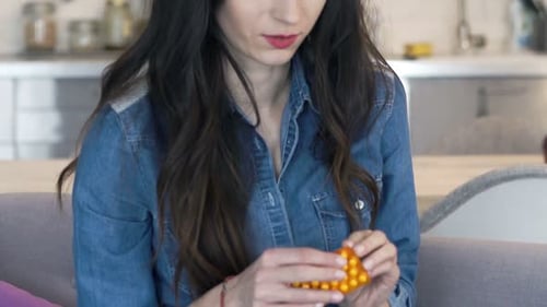 Young Woman Having Headache and Taking Pill Sitting on Sofa at Home 30s