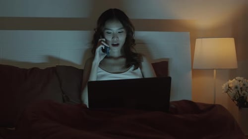 Woman Talking on Phone Using Laptop in Bed