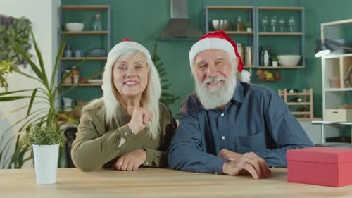 Elderly Couple Waving at the Camera Wearing Santa Hats