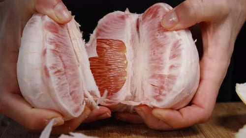 Female hands split a large pomelo fruit into two halves. Slow-motion