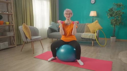 Senior Woman Exercising with Dumbbells on Exercise Ball