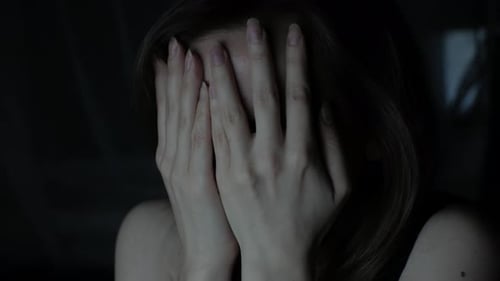 Woman Covers Face with Hands in Darkness