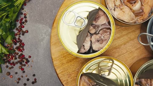 Opening Metal Cans with Canned Fish and Pate on Table Rotating on Wooden Desk Top View Canned Salmon
