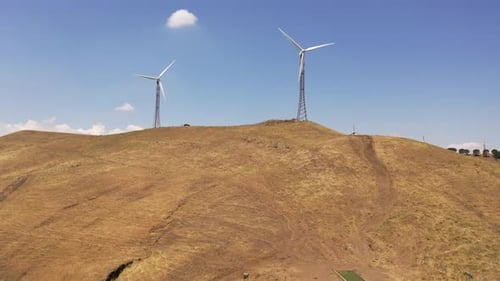 Wind Turbines Spinning Atop Rolling Hills Under Blue Sky