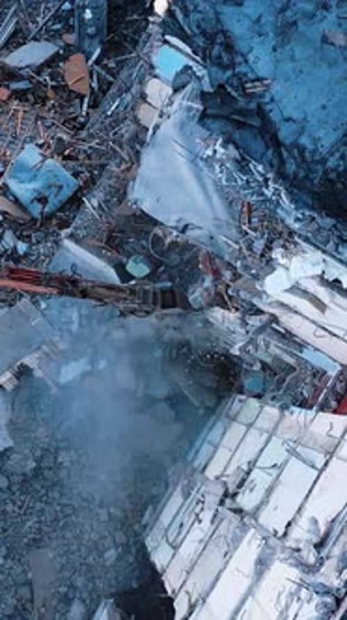 Long claw of an excavator destroys the concrete parts of the building.
